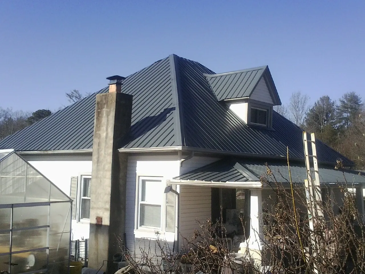 Dark blue standing seam metal roof on a white farmhouse with dormer — Slate & Tile Roof Repair by Roofing Brothers in Hot Springs National Park