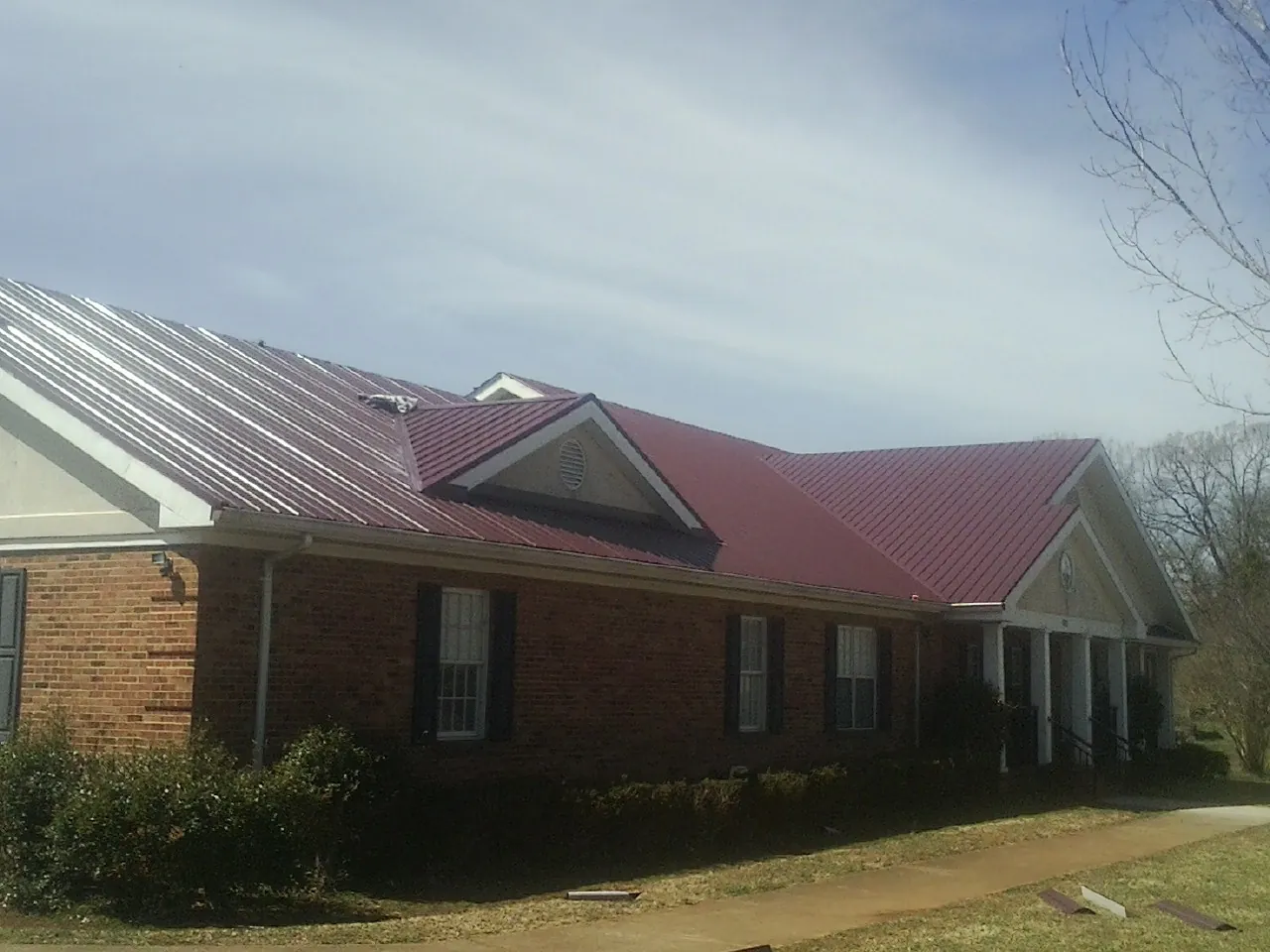 Red metal roof with gabled entries on a long brick building, from a Hail Damage Roof Repair job in Hot Springs National Park