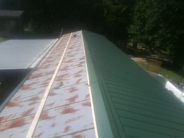 Old rusted panels beside newly installed green metal roofing — Wind Damage Roof Repair by Roofing Brothers in Hot Springs National Park