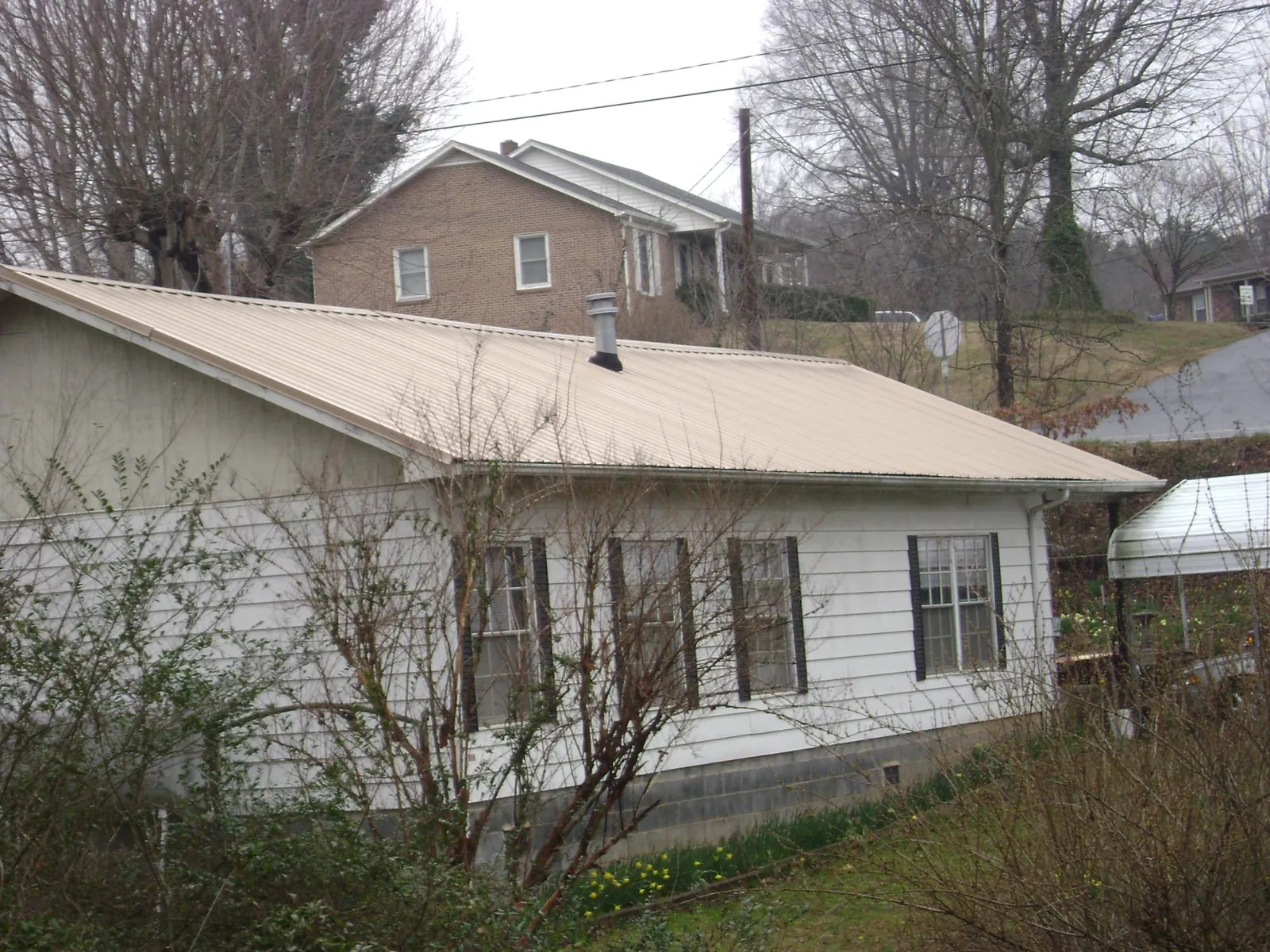 Tan metal roof on a white sided house set into a hillside — Commercial Roofing by Roofing Brothers in Hot Springs National Park