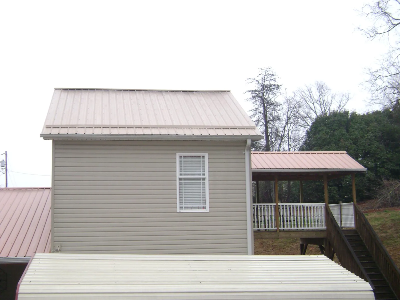 Tan metal roofs on a two story addition and attached porch, from a Roof Replacement job in Hot Springs National Park